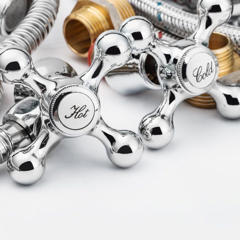 Robinetterie chromée avec poignées "Froid" et "Chaud" sur fond de tuyaux en métal.