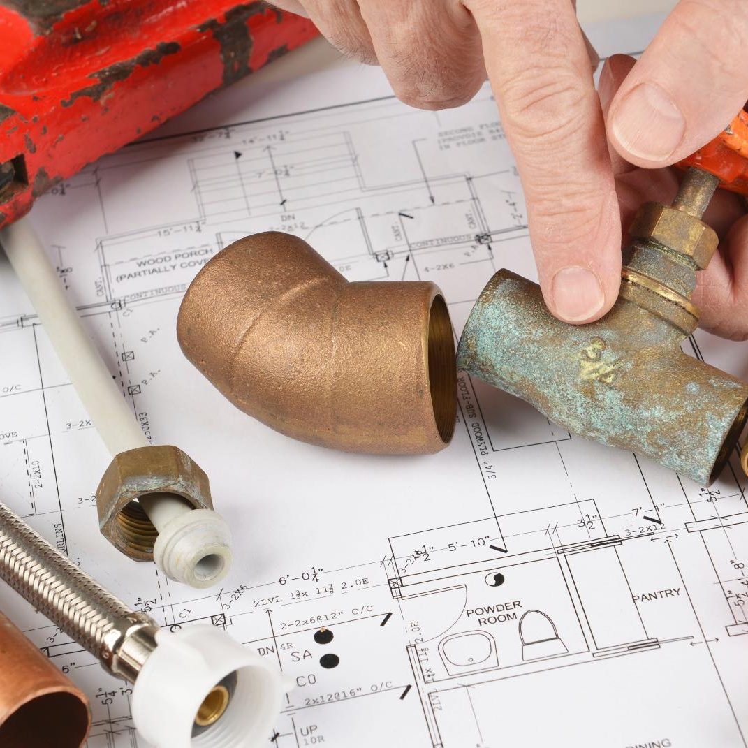 Un plan de plomberie avec des tuyaux, raccords et un main tenant un coude en cuivre.